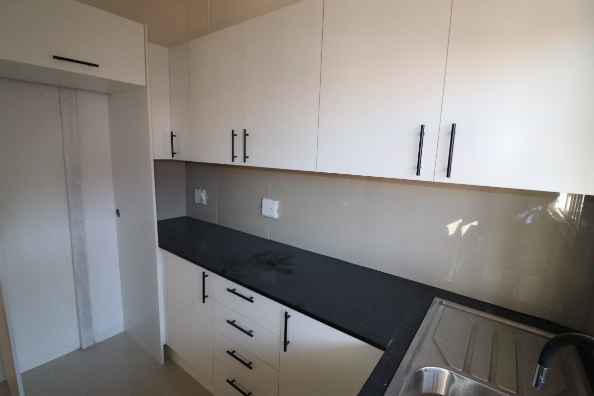 A clean, modern kitchen featuring white cabinetry, dark countertops, and a stainless steel sink, offering a functional and minimalist cooking space.