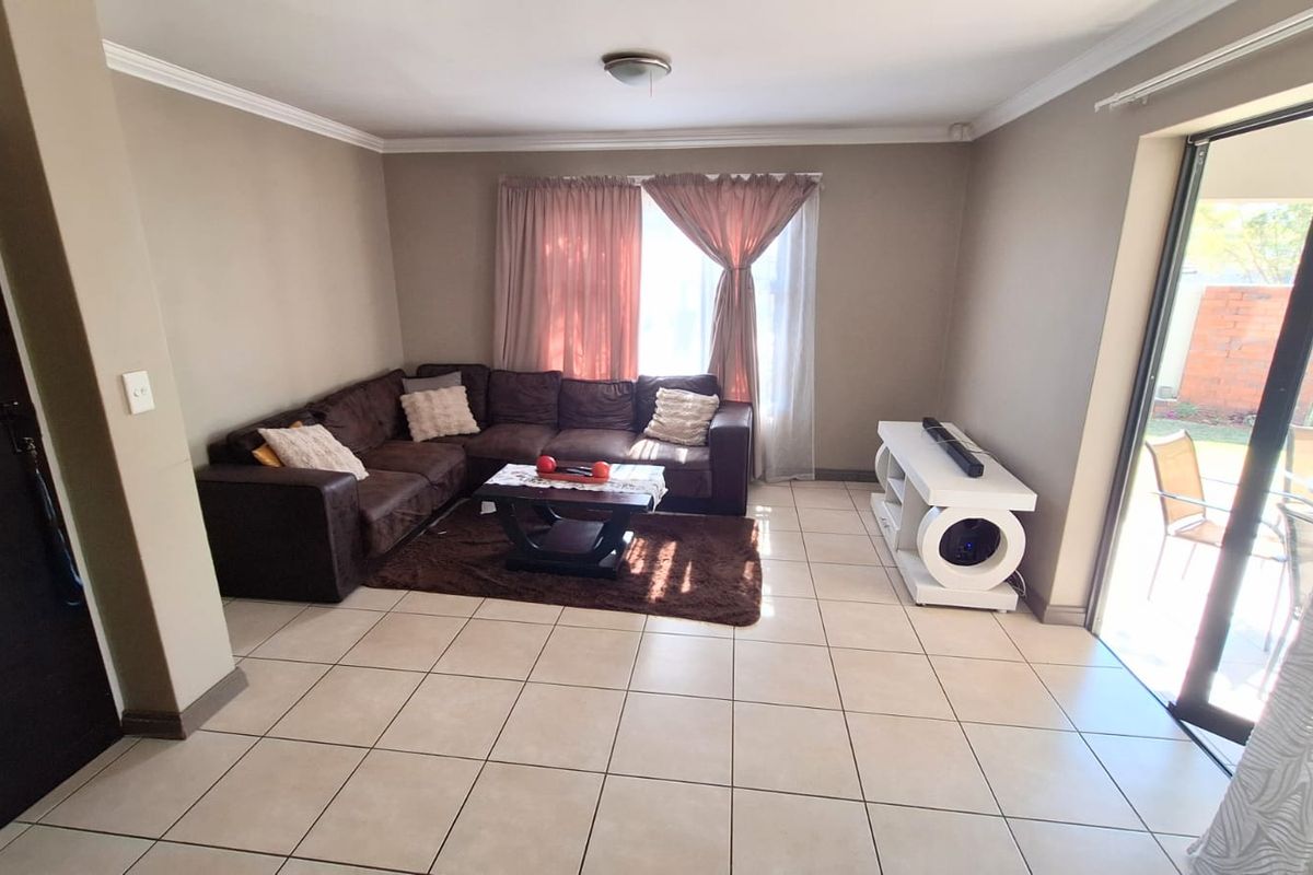 A spacious living room featuring neutral wall tones, ceramic floor tiles, and a large sliding glass door providing access to the outdoor area.