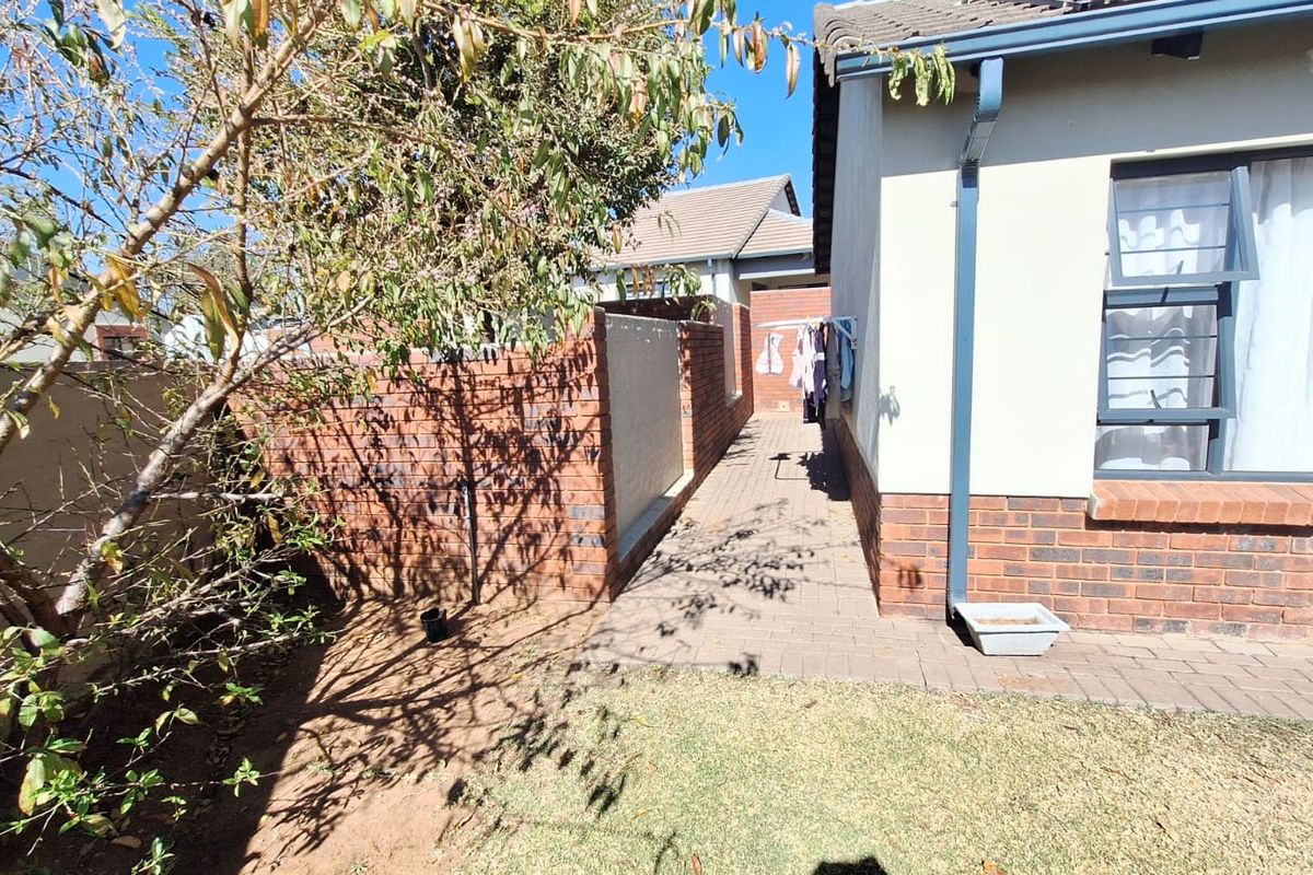 A view of the rear exterior of the house featuring a paved walkway, brick boundary wall, and established garden area.