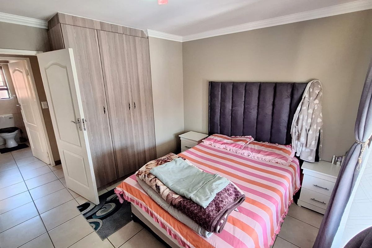 A well-maintained bedroom featuring built-in cupboards, tiled flooring, and direct access to an en-suite bathroom.