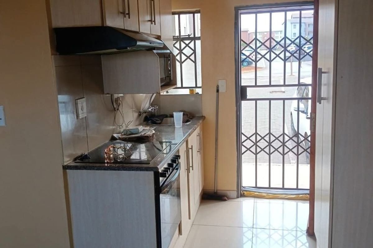 Compact kitchen featuring built-in cabinetry, electric hob, oven, extractor fan, and tiled flooring, with direct access to an exterior security gate.