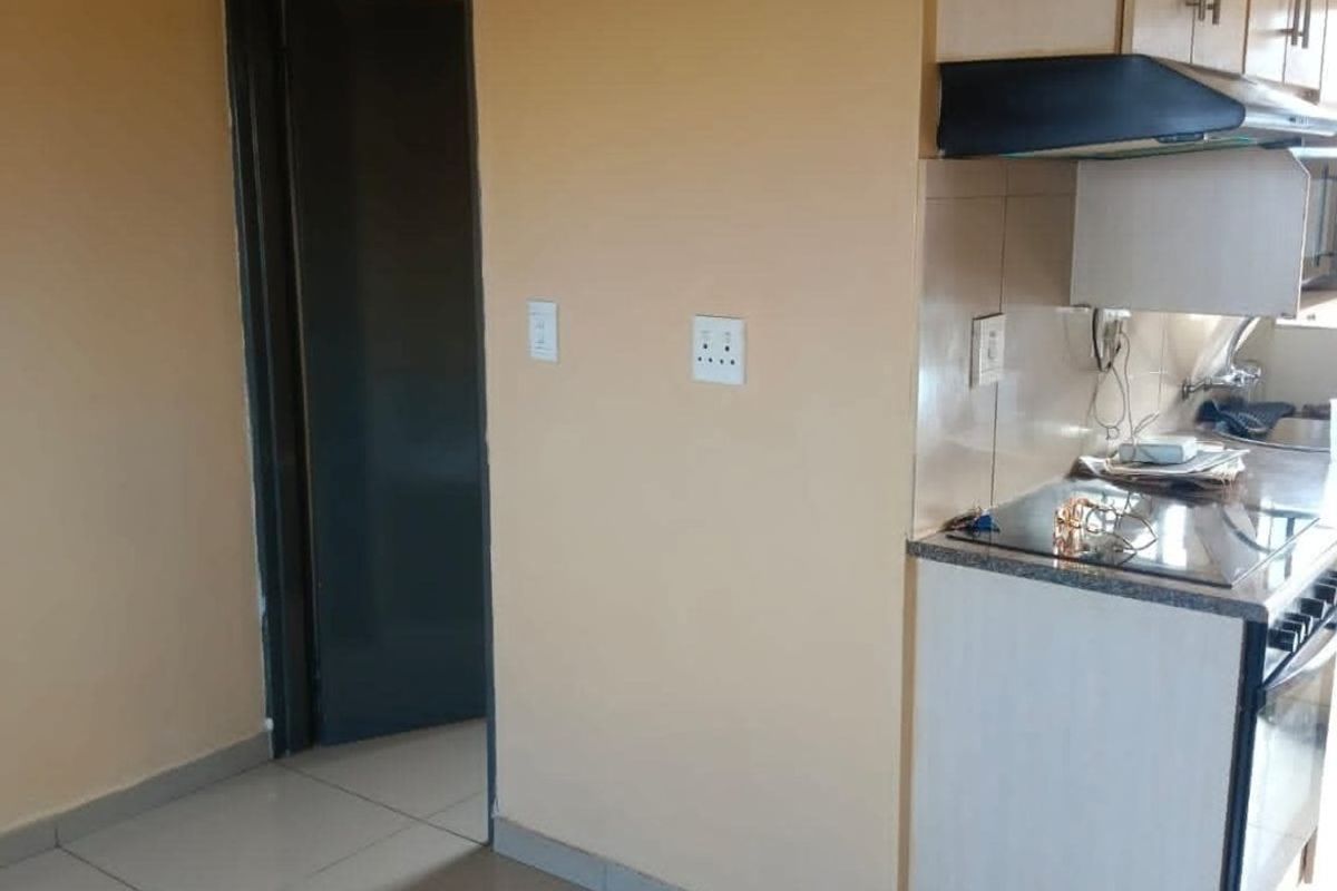 A compact kitchen area featuring built-in cabinetry, an electric hob, and an extractor fan, finished with neutral wall paint and tiled flooring.