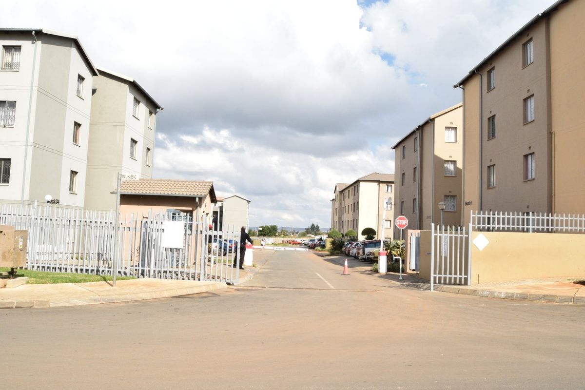 View of the secure entrance and access road to a multi-story apartment complex with perimeter fencing and a guard house.