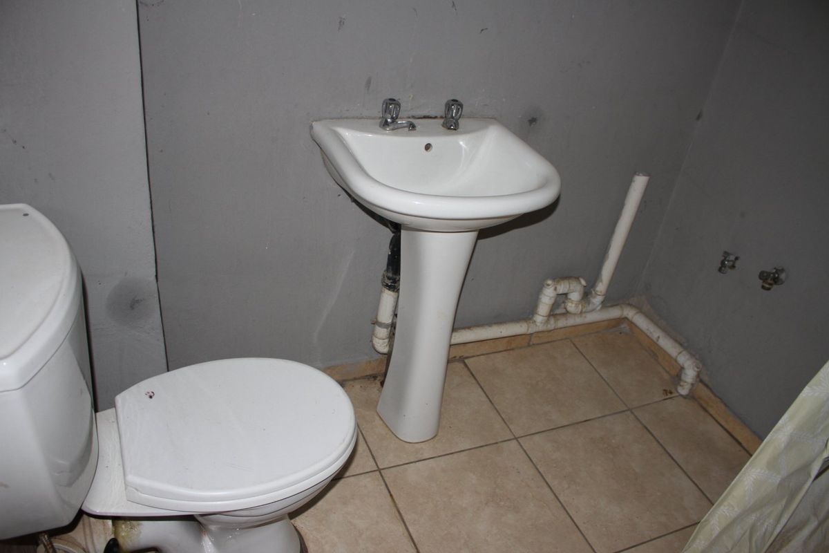 A basic bathroom featuring a pedestal basin and toilet with exposed plumbing and unfinished wall surfaces, requiring renovation to improve functionality and aesthetics.