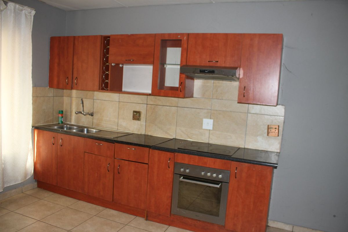A functional kitchen featuring wooden cabinetry, a built-in oven with electric hob, extractor fan, and tiled backsplash, offering a practical layout for daily use.