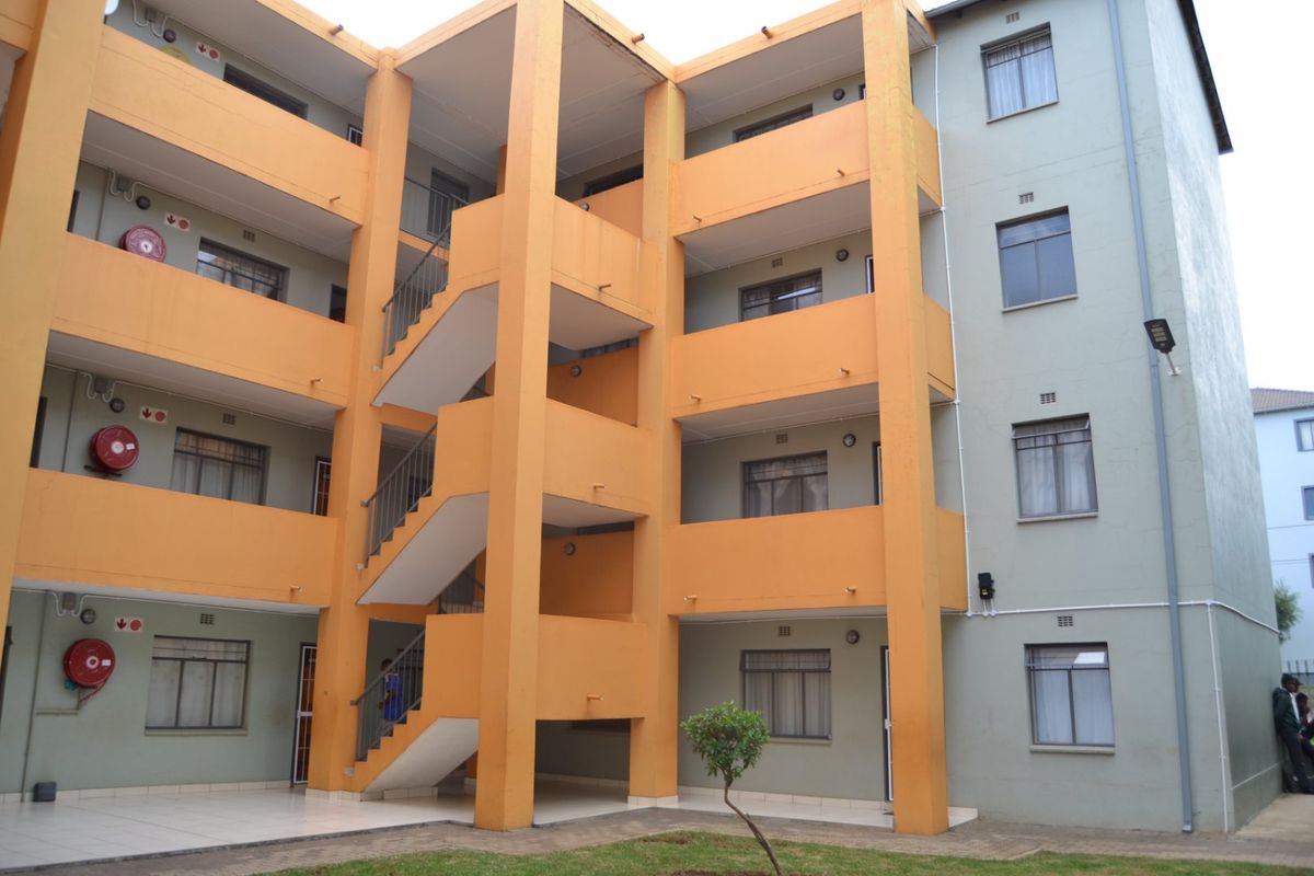 Exterior view of a multi-story apartment building featuring open-air staircases, balconies, and a shared ground-level courtyard area.