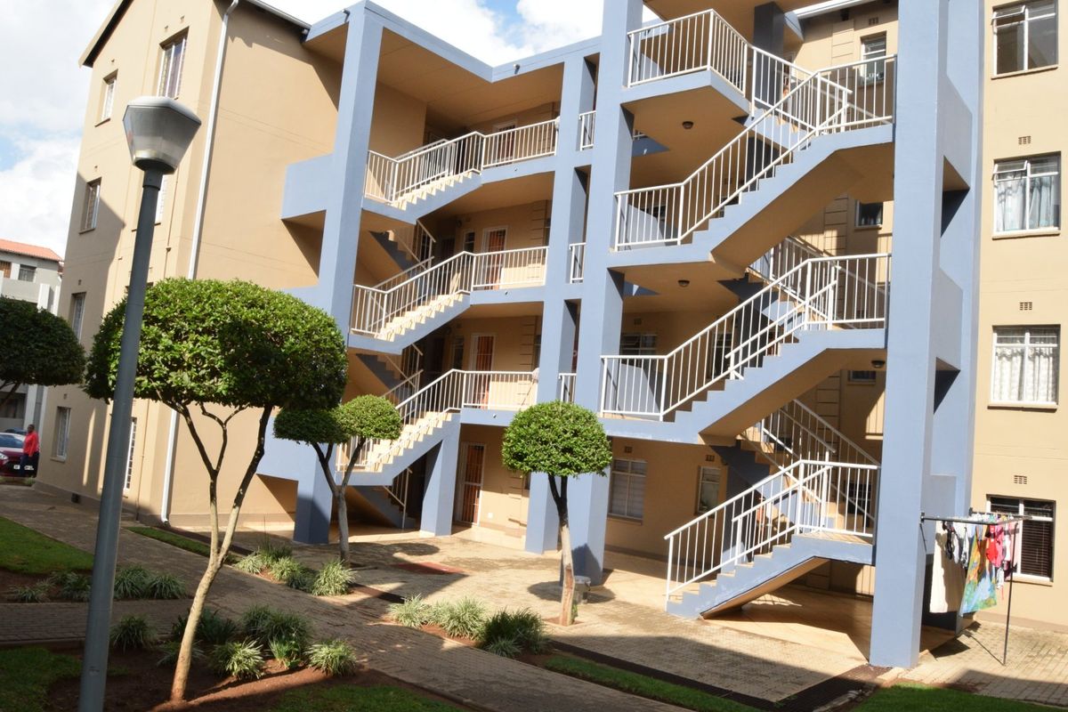 Exterior view of an apartment complex featuring a multi-level staircase, paved courtyard, and landscaped garden area.