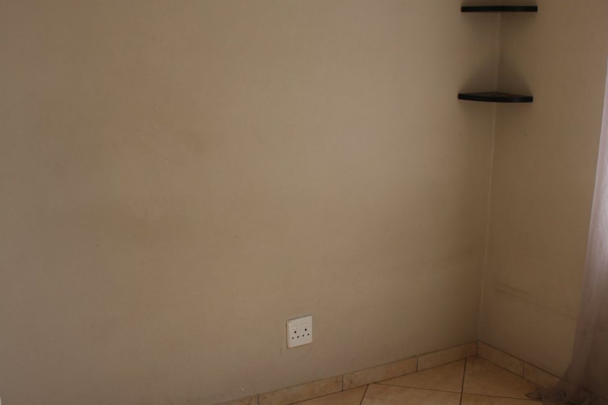 A vacant bedroom featuring neutral tiled flooring, corner shelving, and a wall-mounted curtain rod, offering a blank canvas for personalization.