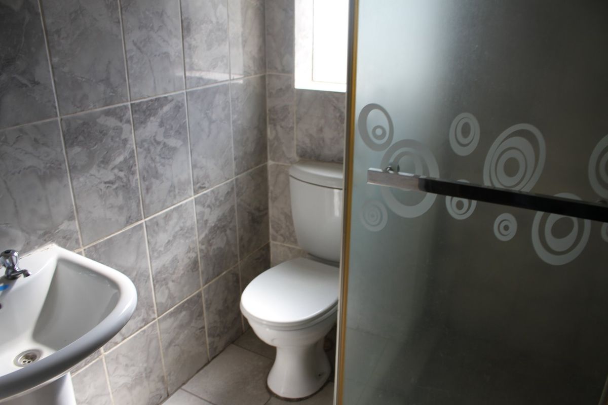 A compact bathroom featuring a pedestal basin, toilet, and a shower enclosure with frosted glass, finished with grey marble-effect wall tiles.