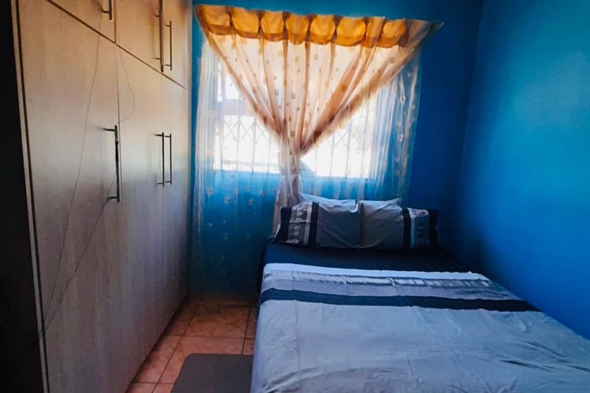 A compact bedroom featuring built-in wooden cupboards, tiled flooring, and security bars on the window.