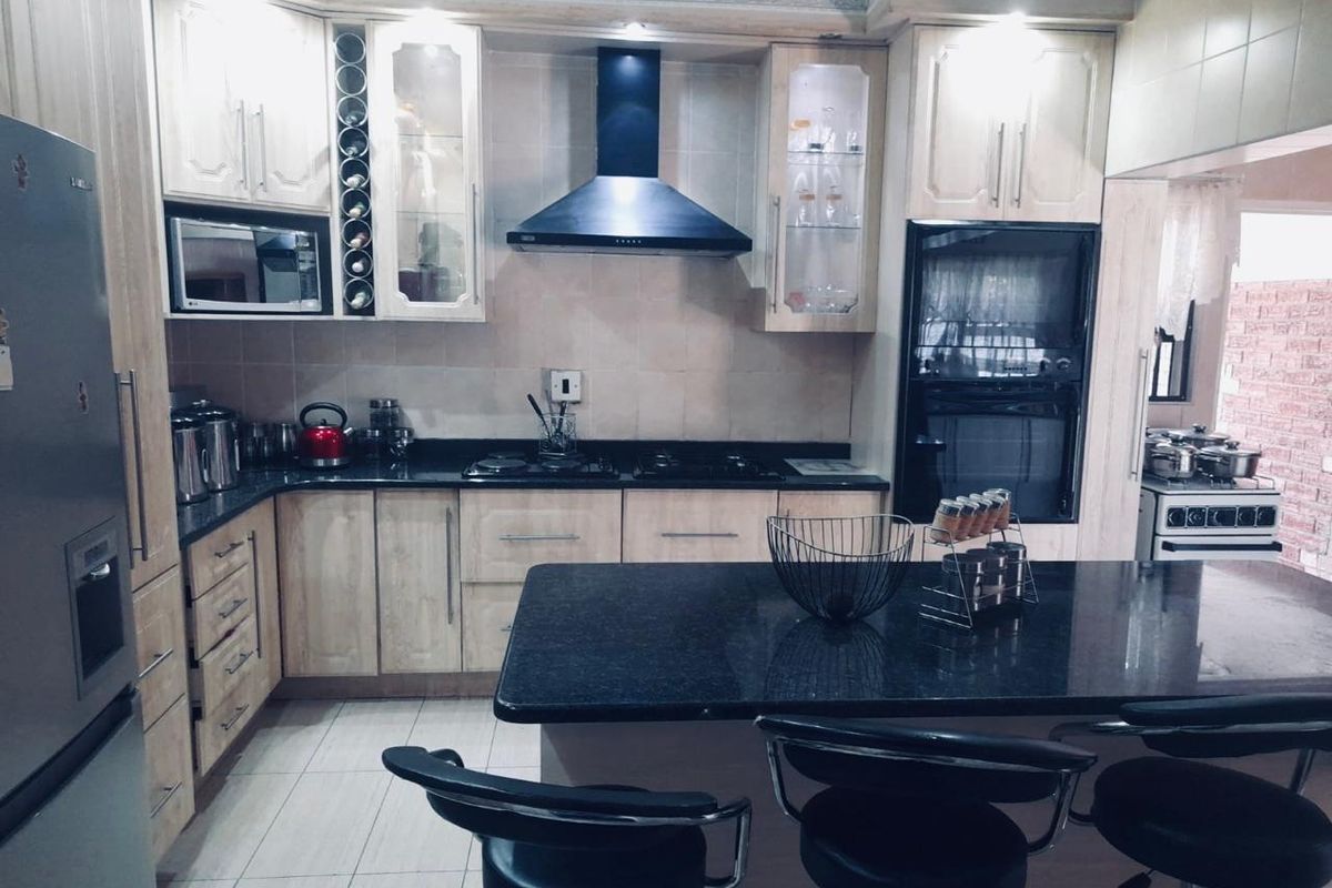 A functional kitchen featuring light wood cabinetry, dark granite countertops, a central island, and integrated appliances including an oven and extractor fan.