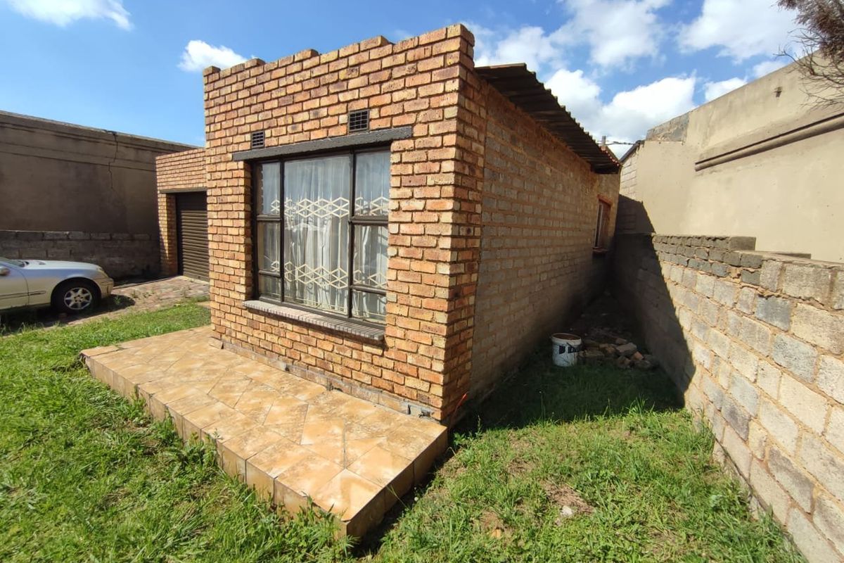 Rear view of a face brick house featuring a small tiled patio and metal window frames set within a fenced yard.