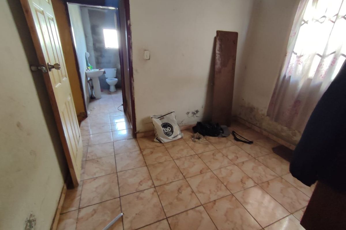 A vacant bedroom featuring tiled flooring and an adjoining bathroom, currently requiring significant cosmetic repairs and wall maintenance.