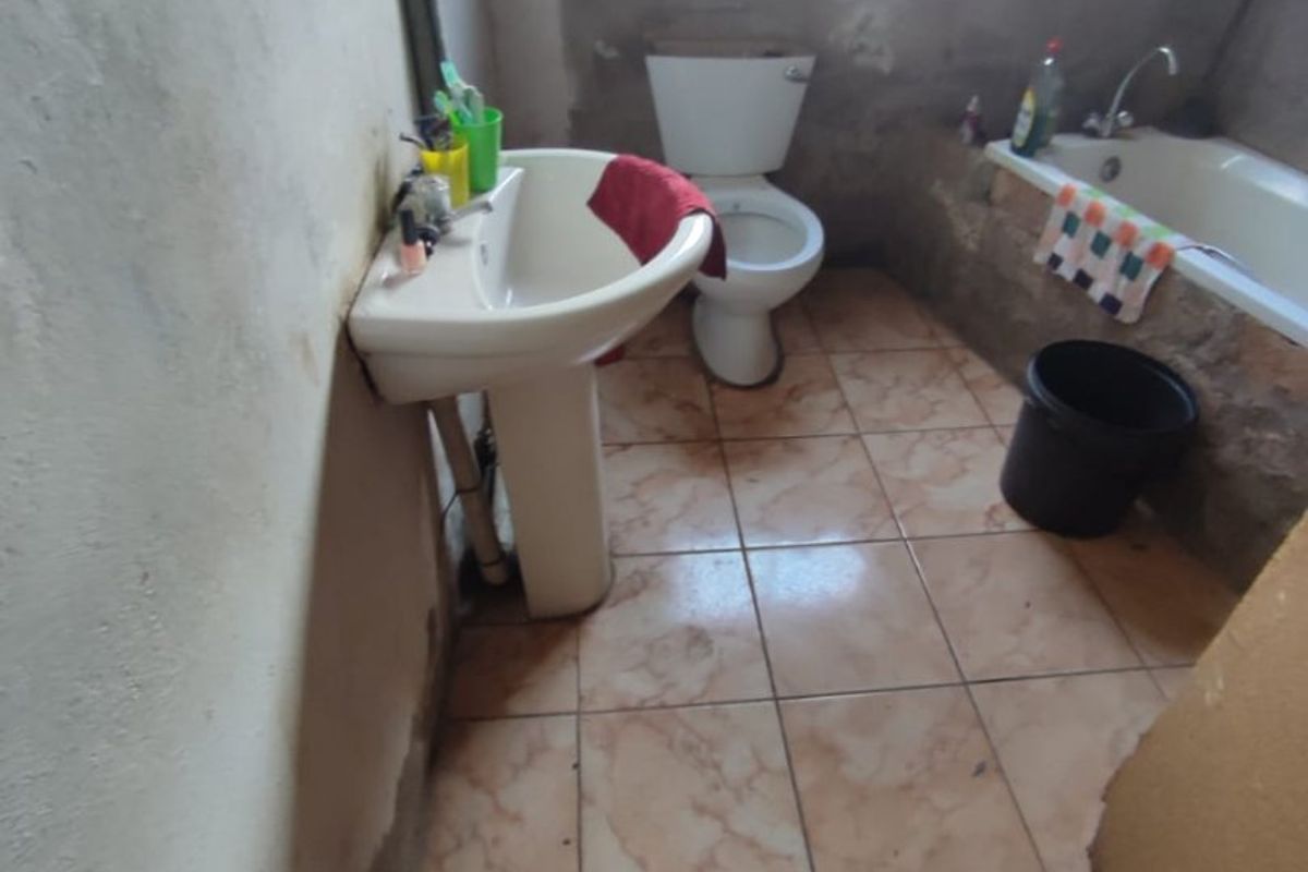 A bathroom featuring a pedestal basin, toilet, and bathtub with tiled flooring. The room requires significant finishing and renovation to improve its condition.
