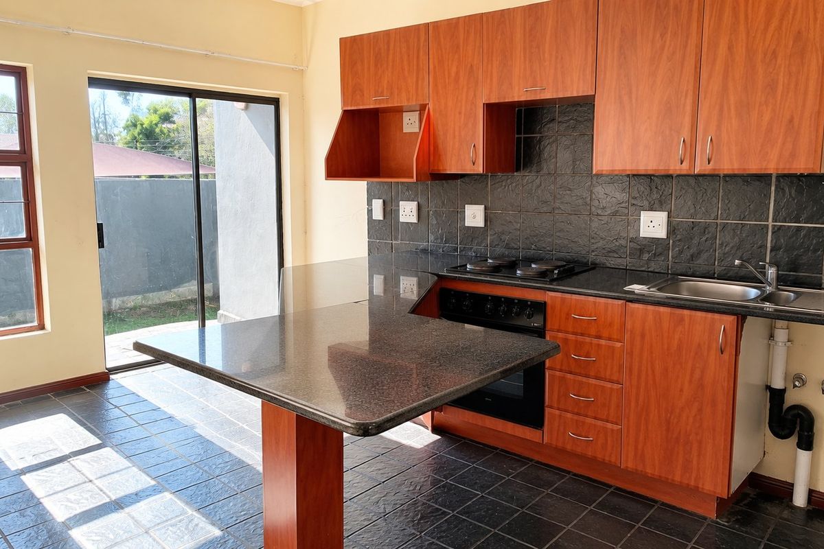 A functional kitchen featuring wood-finish cabinetry, granite countertops, built-in oven and hob, and direct access to an outdoor area via a sliding glass door.