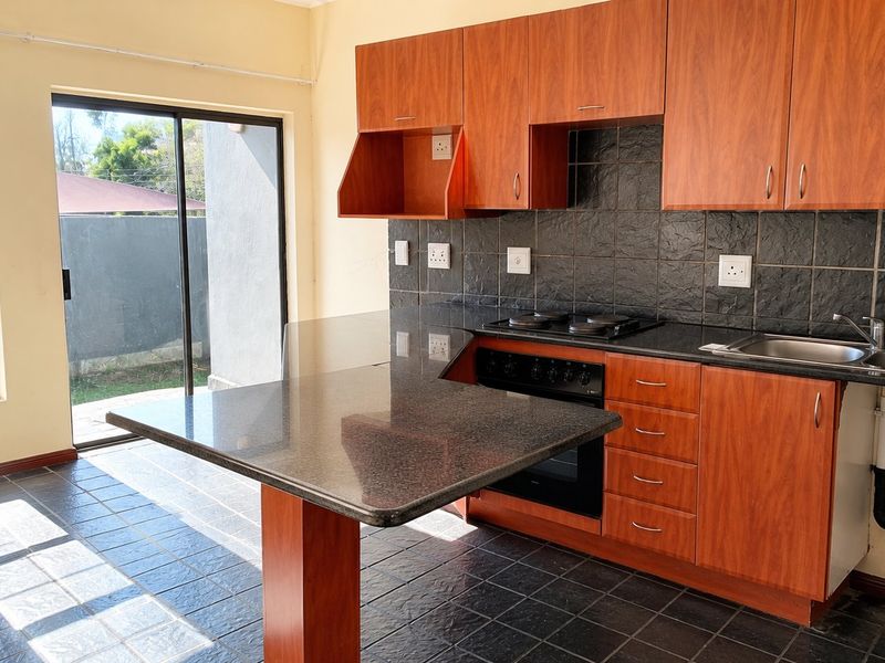 A functional kitchen featuring wood-finish cabinetry, granite countertops, built-in oven and hob, and direct access to an outdoor area via a sliding glass door.