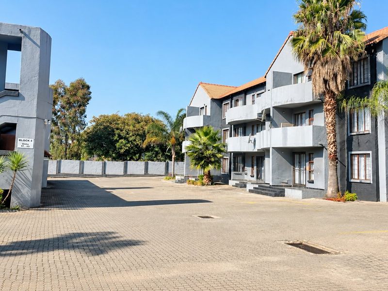 Exterior view of an apartment complex featuring a paved parking area, multi-level balconies, and a concrete stairwell structure.