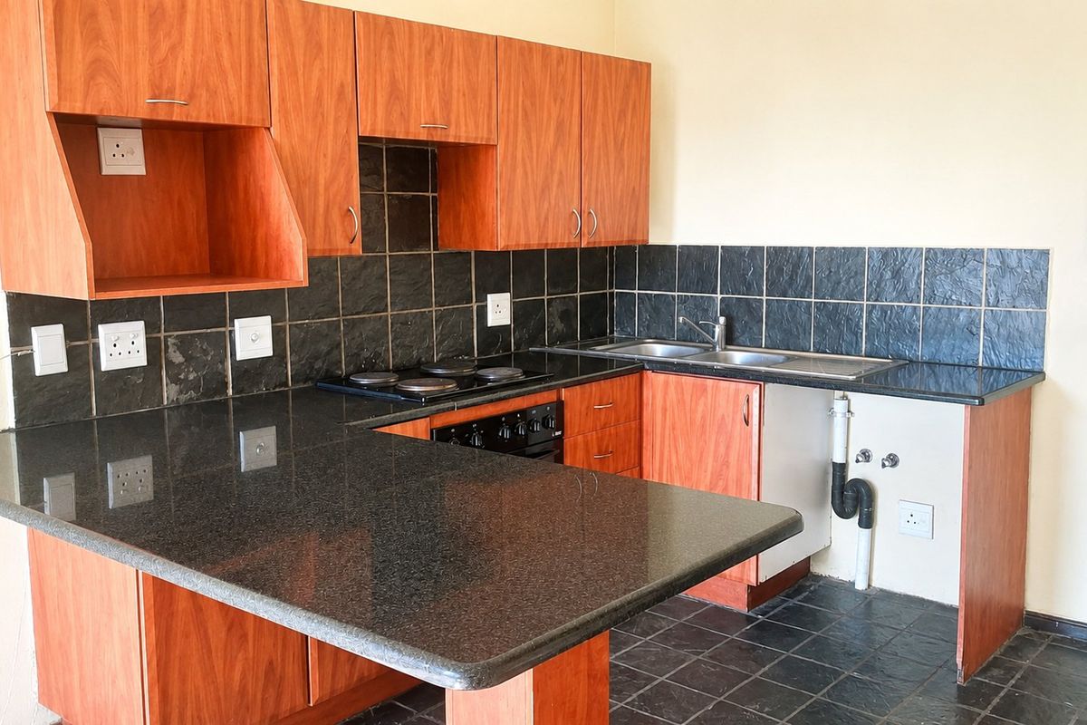 Functional kitchen featuring wood-look cabinetry, granite countertops, integrated electric hob and oven, and a double sink with tiled backsplash and flooring.