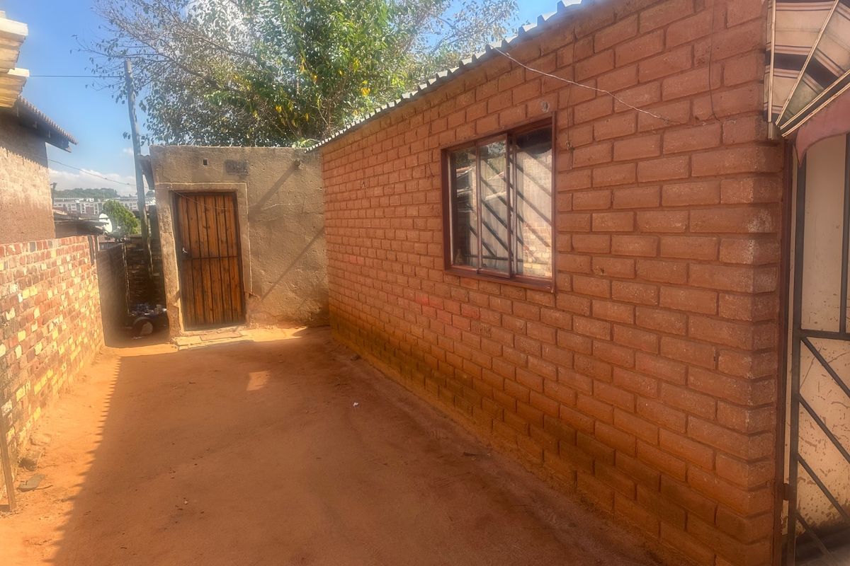 A view of the rear exterior area featuring exposed brick walls, a timber door, and a corrugated roof structure.