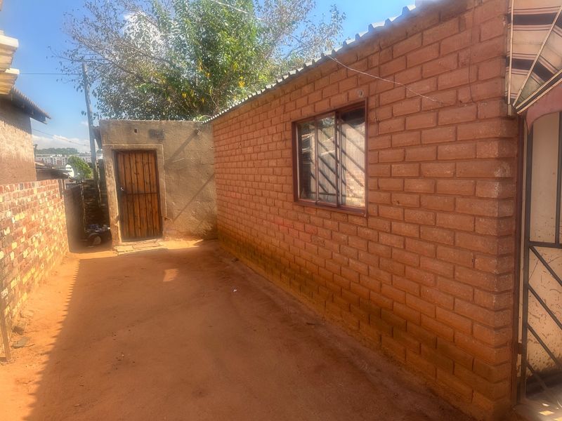 A view of the rear exterior area featuring exposed brick walls, a timber door, and a corrugated roof structure.