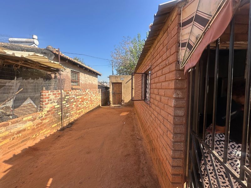 A side passage or rear exterior area featuring exposed brick walls, security bars on windows, and an unpaved ground surface.