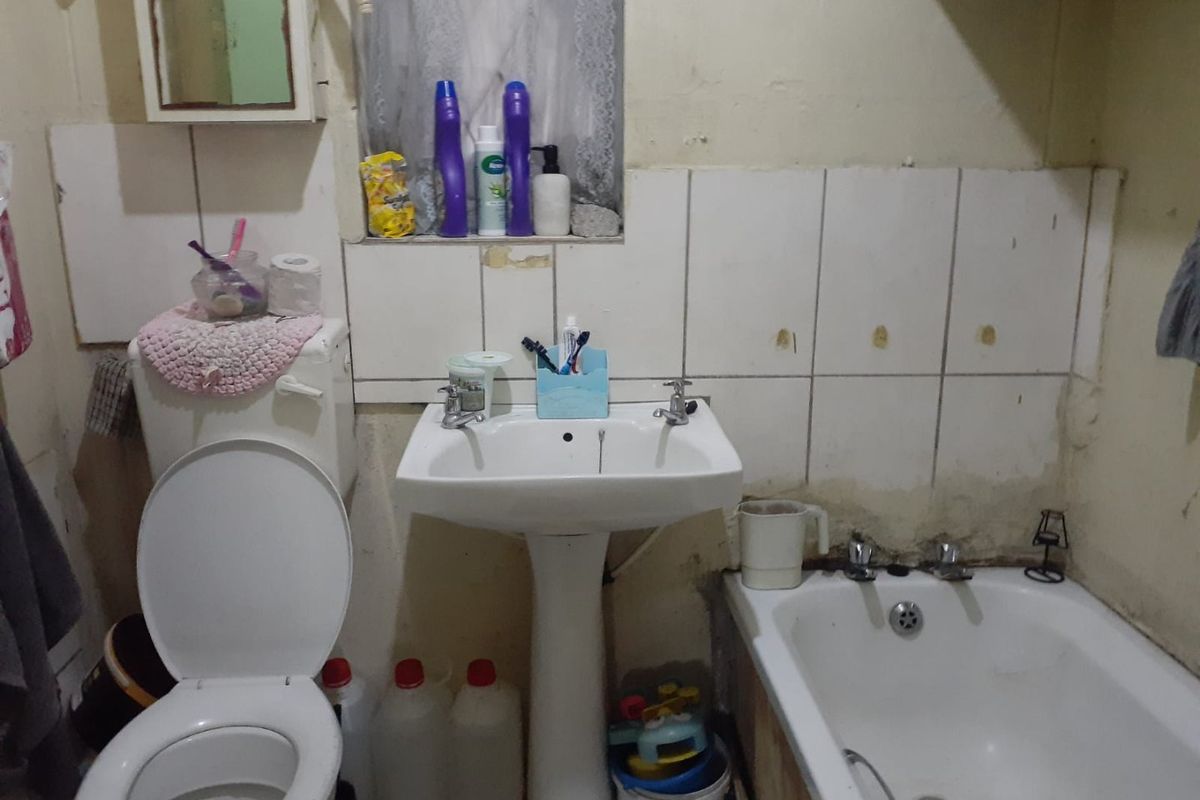 A dated bathroom featuring a pedestal basin, toilet, and bathtub with visible wear to the wall tiles and paint finishes.