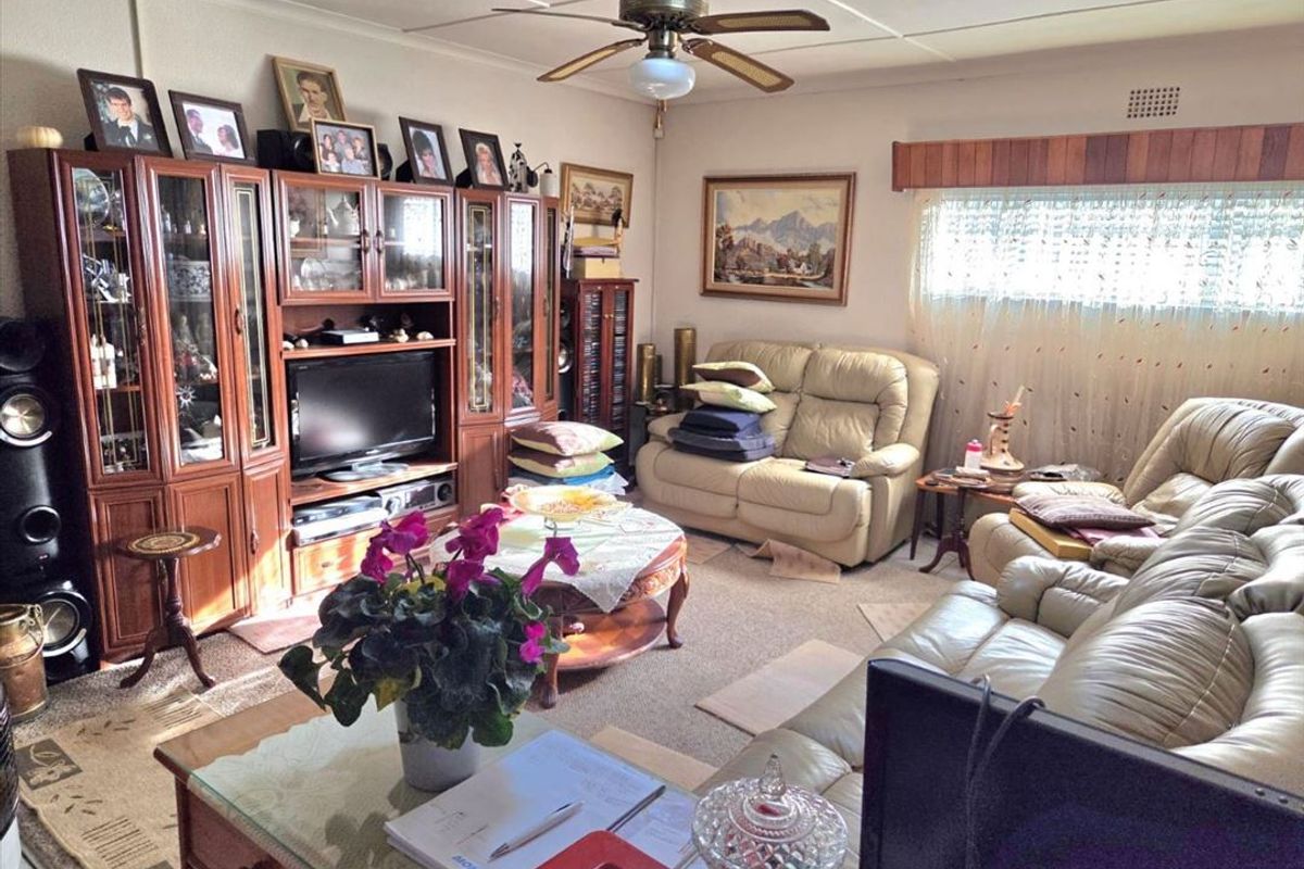 A traditional living room featuring a ceiling fan, carpeted flooring, and a window pelmet, offering a comfortable and functional space.