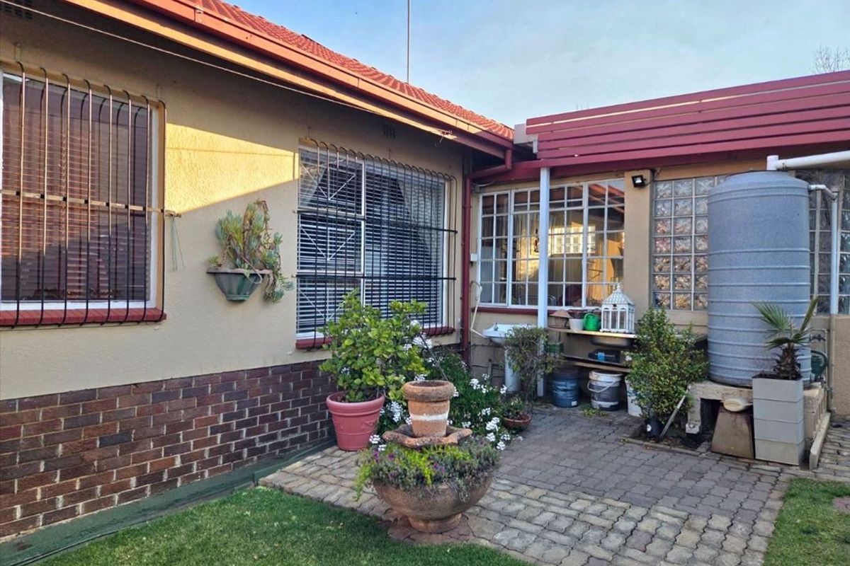 Rear exterior view featuring a paved patio area, security bars on windows, and a water tank against a brick and plaster facade.