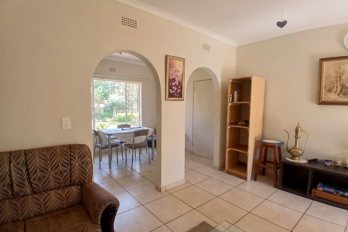 A living area featuring ceramic floor tiles and distinctive arched doorways leading to an adjacent dining space with garden views.