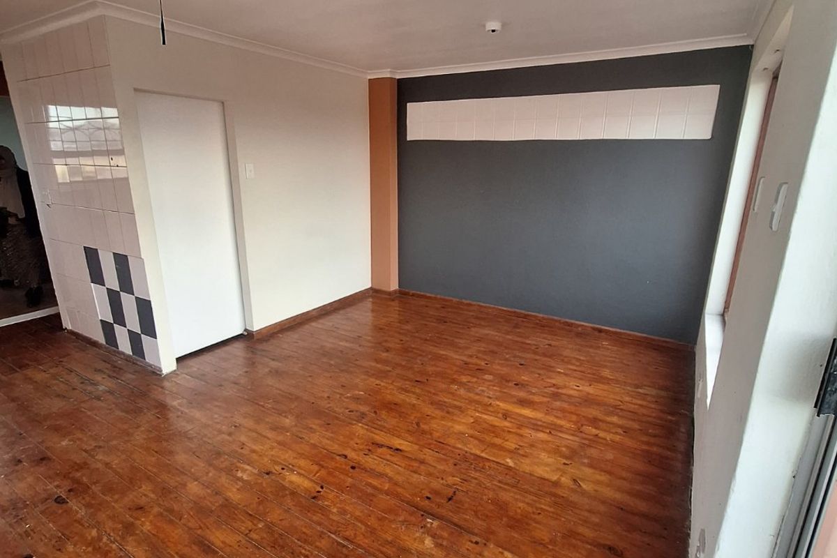 An empty living room featuring original hardwood flooring, a dark accent wall, and a ceiling access hatch.