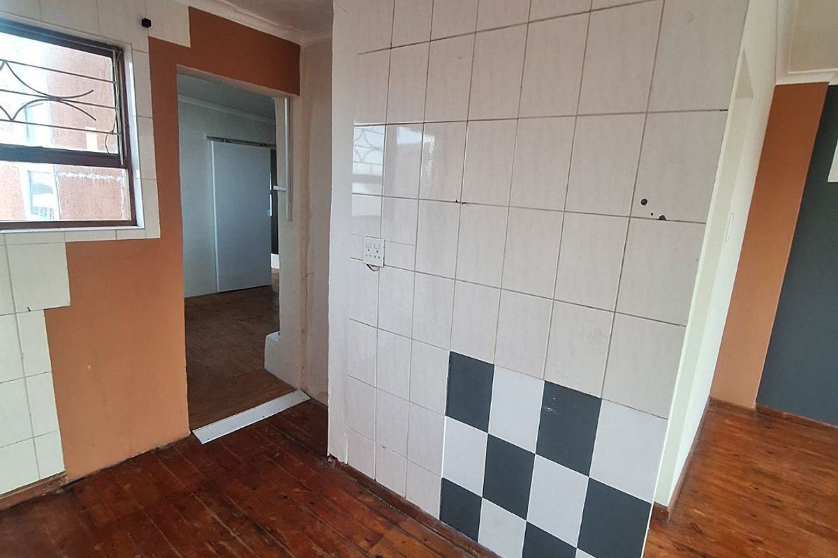 An empty kitchen area featuring timber flooring and partially tiled walls, currently requiring renovation and finishing to reach its full potential.