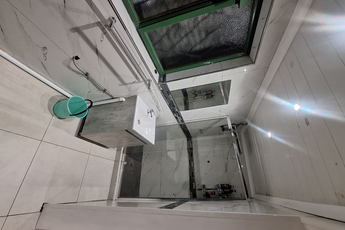 A modern bathroom featuring a glass shower enclosure, vanity basin, and tiled finishes, though some plumbing remains exposed.