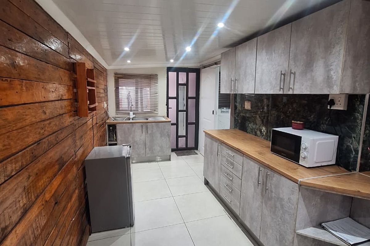 A functional kitchen featuring grey cabinetry, timber wall cladding, tiled flooring, and a stainless steel sink with ample counter space.