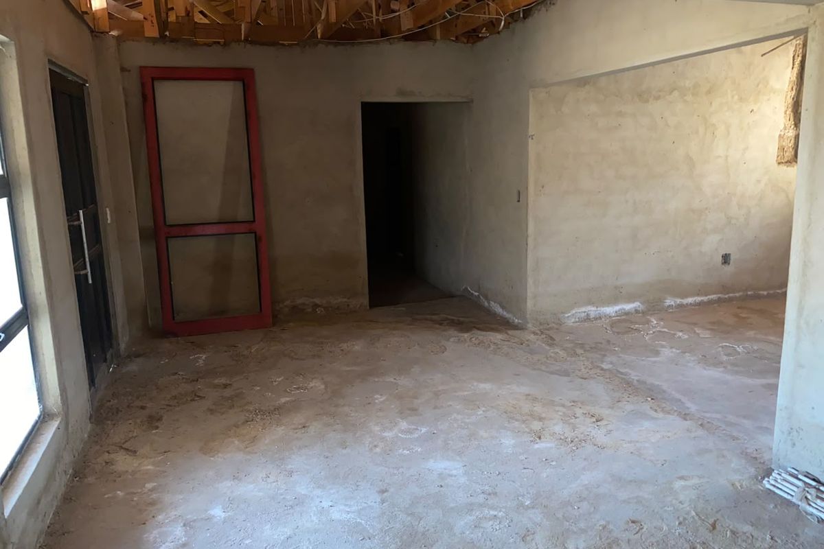 An interior space currently under renovation, featuring exposed timber roof trusses, unfinished plaster walls, and cement screed flooring, offering a blank canvas for completion.