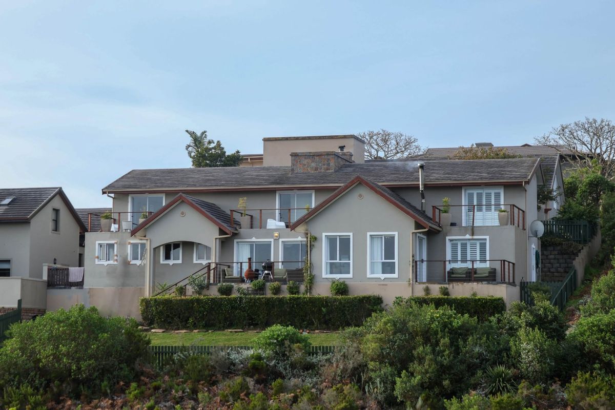 Rear elevation of a multi-level residential property featuring a tiled roof, stone chimney, upper-level balconies, and well-maintained garden landscaping.