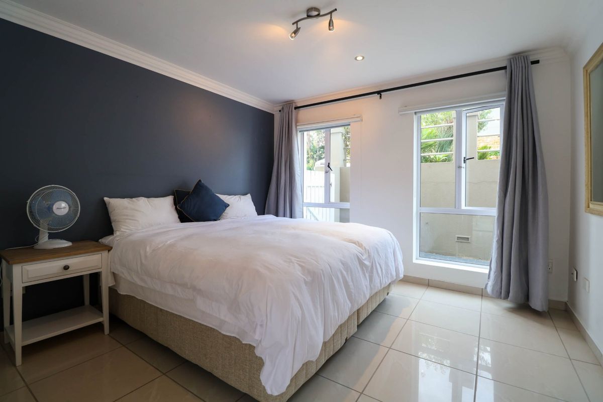 A well-maintained bedroom featuring tiled flooring, a dark accent wall, and large casement windows that provide natural light.