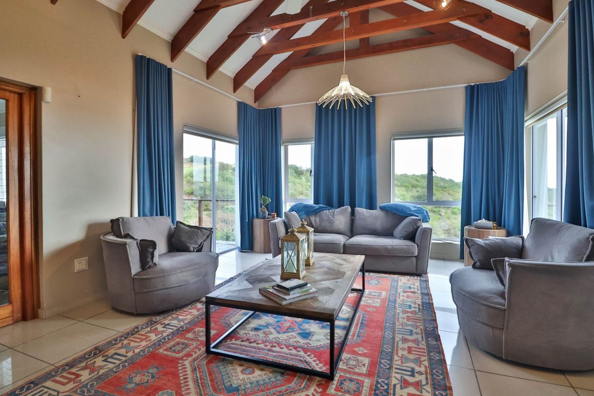Spacious living room featuring a high vaulted ceiling with exposed timber rafters, tiled flooring, and large windows providing ample natural light and scenic views.