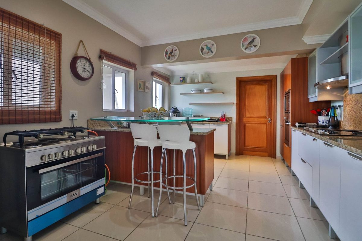 A functional kitchen featuring granite countertops, a gas stove, built-in oven, and a breakfast bar with tiled flooring and wooden cabinetry.