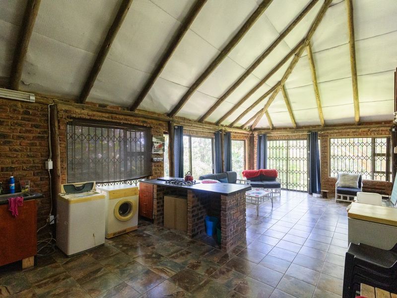 Spacious open-plan living area featuring exposed brick walls, timber rafters, and a central brick kitchen island with a built-in gas hob.