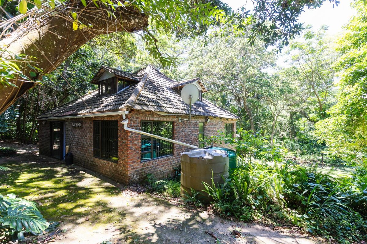 A rustic brick cottage exterior nestled in a wooded setting, featuring a tiled roof, dormer windows, and an integrated rainwater collection system.
