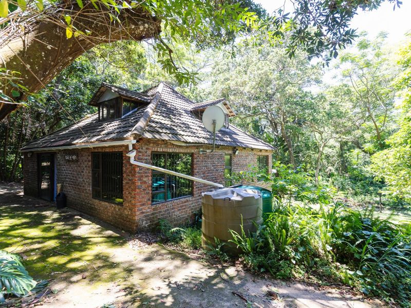 A rustic brick cottage exterior nestled in a wooded setting, featuring a tiled roof, dormer windows, and an integrated rainwater collection system.