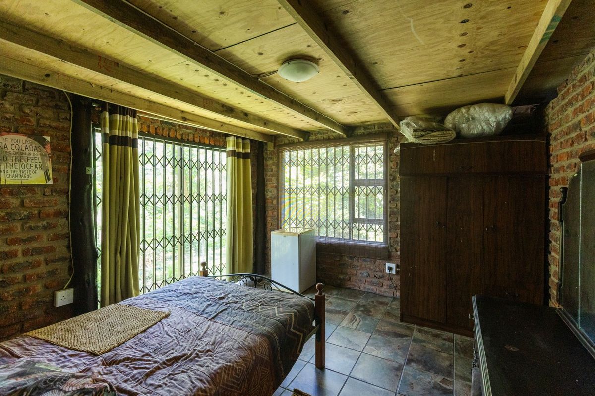 Rustic bedroom featuring exposed brick walls, timber beam ceiling, tiled flooring, and secure window and door grilles.