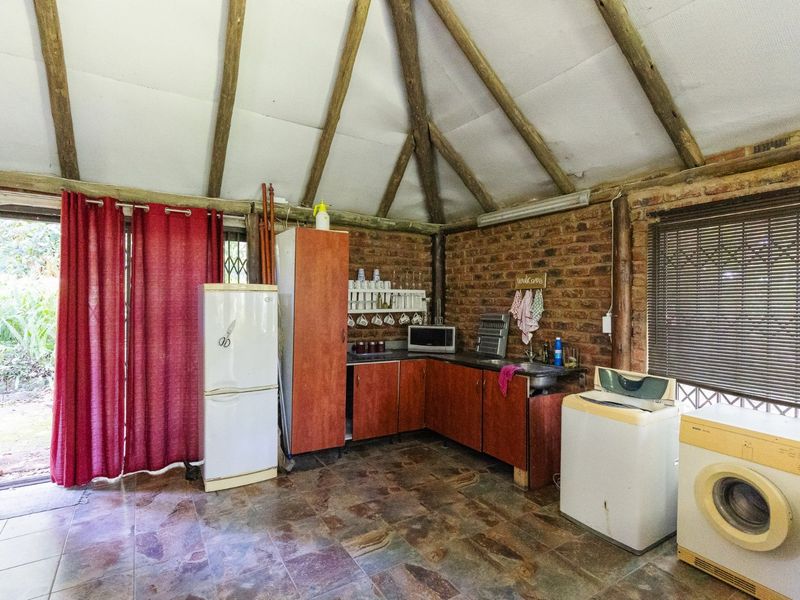 Rustic kitchen area featuring exposed brick walls, timber rafters, tiled flooring, and functional built-in cabinetry with direct access to the garden.