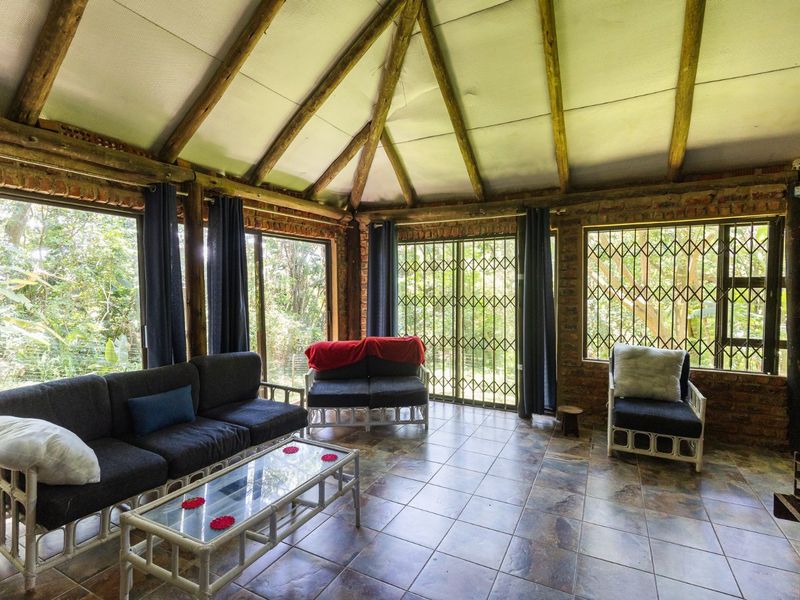 A rustic living room featuring exposed timber rafters, brick walls, and large sliding glass doors with security gates, offering views of the surrounding garden.