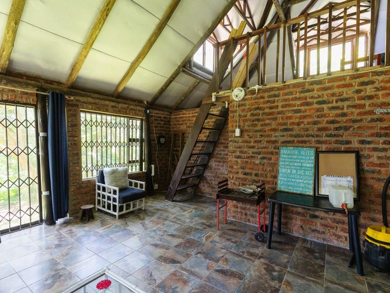 Rustic living area featuring exposed brick walls, timber rafters, tiled flooring, and a mezzanine level accessed by a timber staircase.