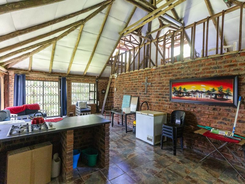 Open-plan living area featuring exposed brick walls, timber rafters, and a mezzanine level, incorporating a kitchen island with a built-in gas hob.