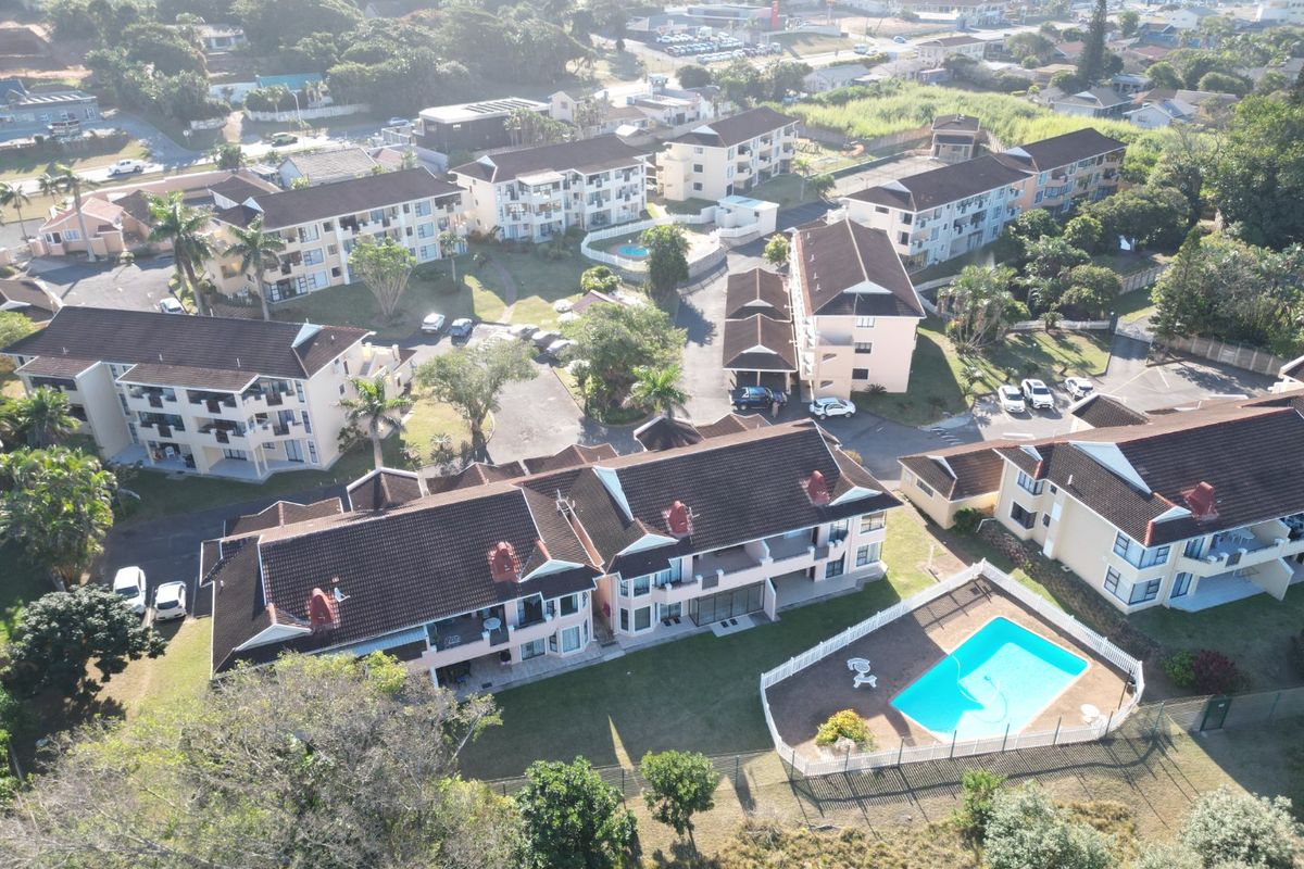 Aerial view of the apartment complex featuring multiple residential blocks, communal swimming pool, landscaped gardens, and paved parking areas.