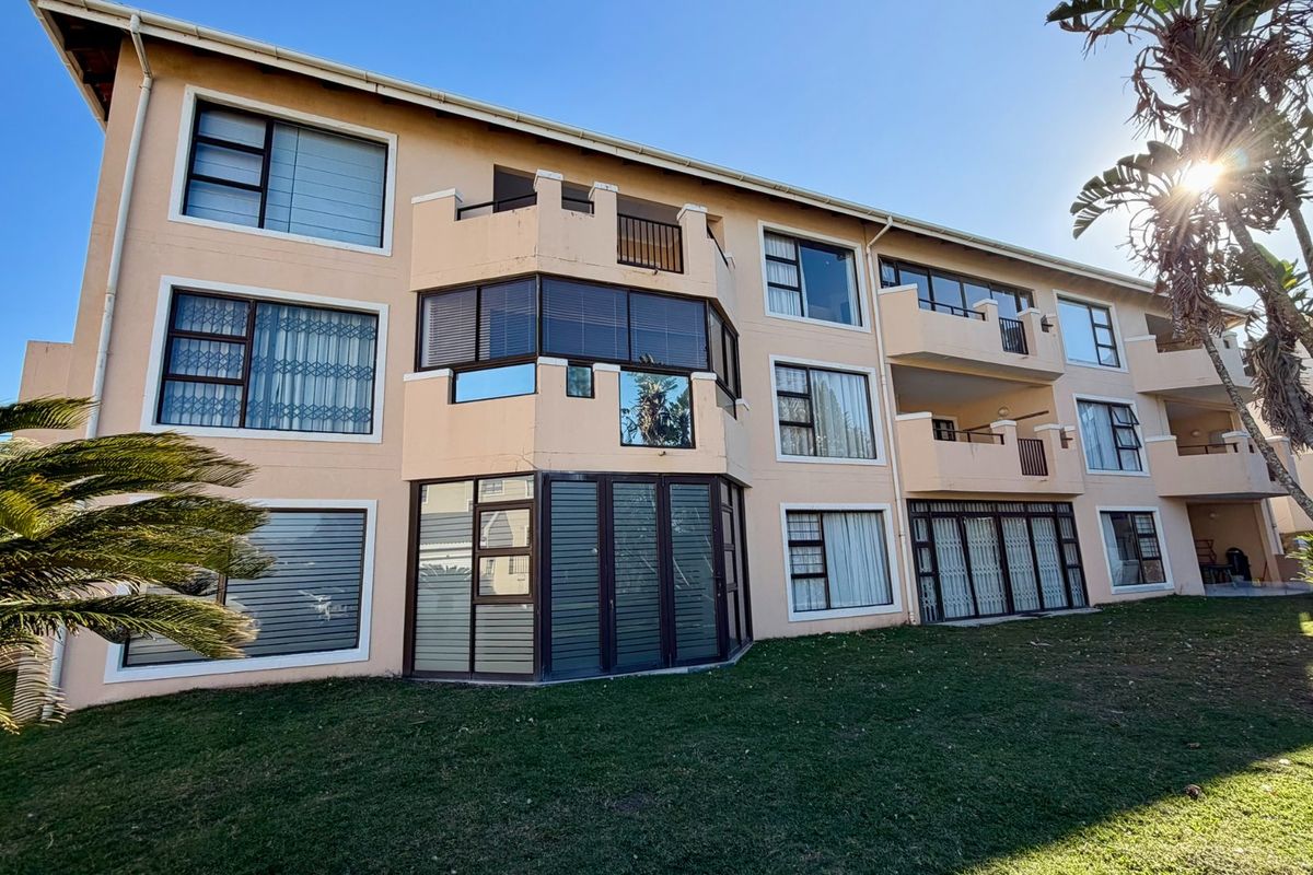 Rear elevation of a multi-story apartment complex featuring balconies, large sliding doors, and established garden space.