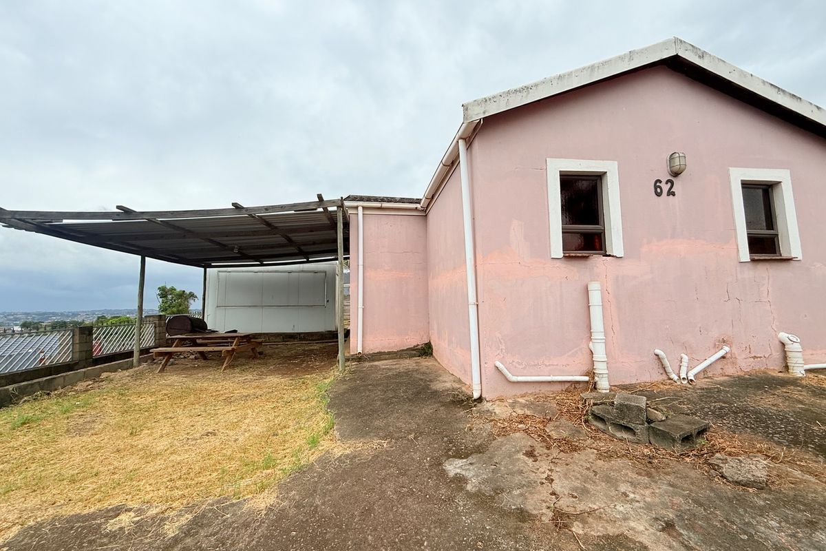 Rear exterior view of the property featuring a covered patio area, concrete paving, and visible exterior wall finishes requiring maintenance.
