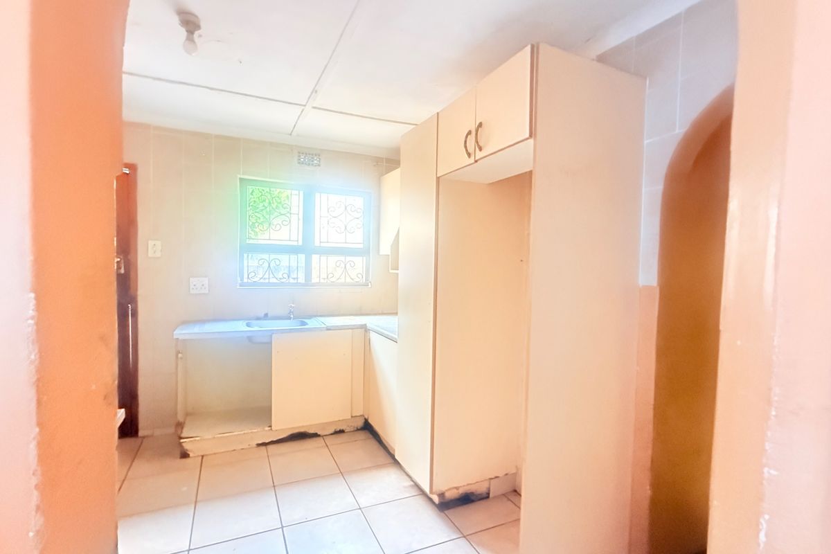 A dated, empty kitchen featuring built-in cabinetry, tiled flooring, and a stainless steel sink, requiring cosmetic updates and repairs.